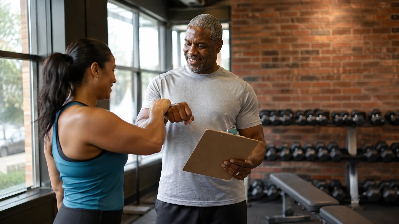 Two anonymous training partners reviewing a workout card and fist-bumping in a bright gym
