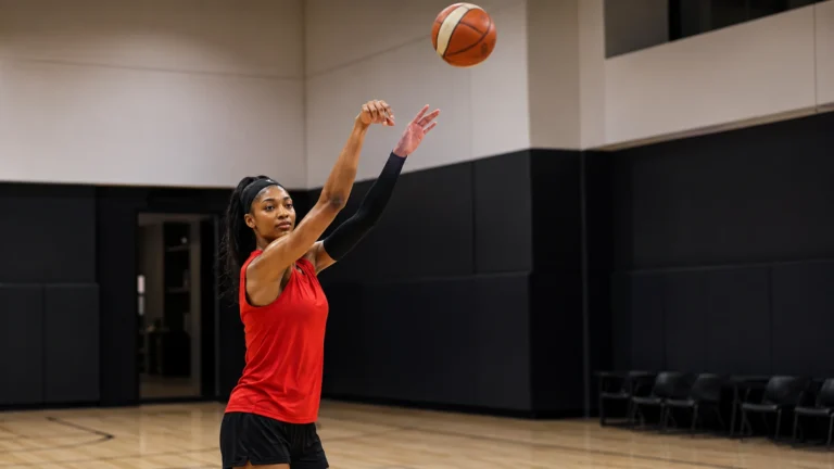 Angel Reese practices a three-point jump shot alone in an unbranded indoor basketball gym.