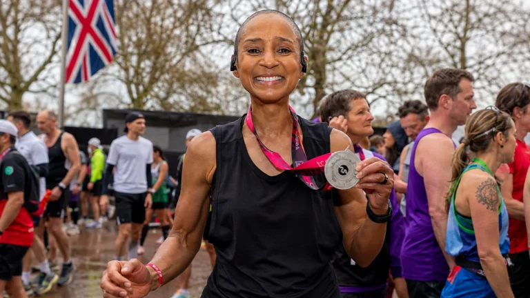Adele Roberts smiles and holds a marathon finisher medal in a crowded outdoor finish area.