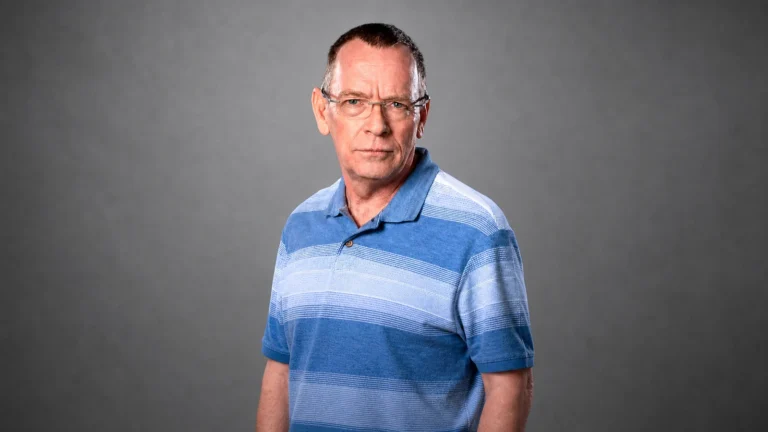 Facebook-derived studio portrait of Adam Woodyatt wearing glasses and a blue striped polo.