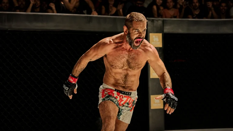 Facebook-derived film-scene portrait of Daniel MacPherson wearing combat gloves inside a cage.