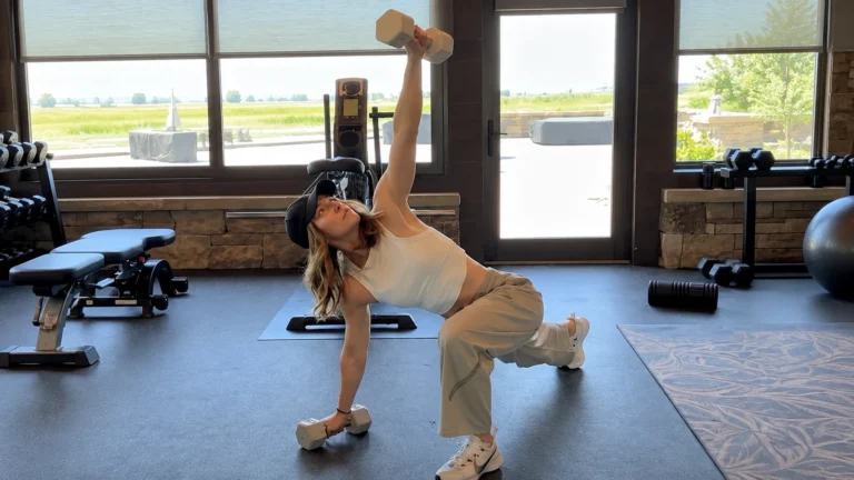 Jessica Biel performing a rotating half-kneeling dumbbell exercise in a home gym