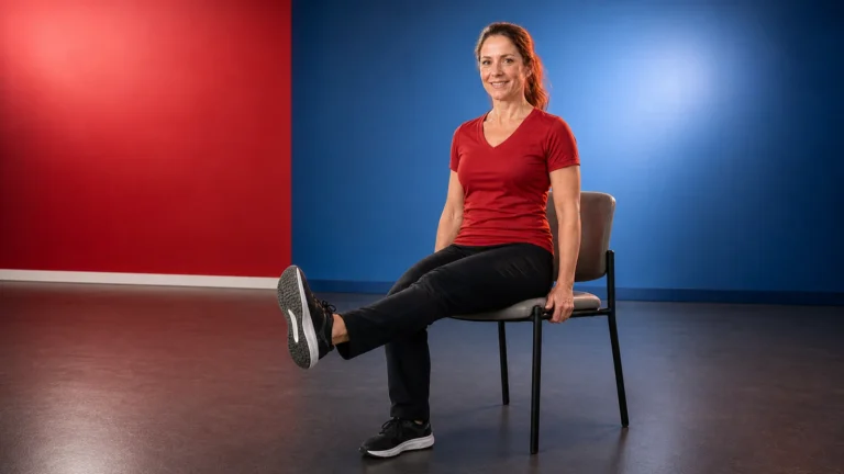 Woman seated on a chair with one leg extended in a red and blue exercise room.