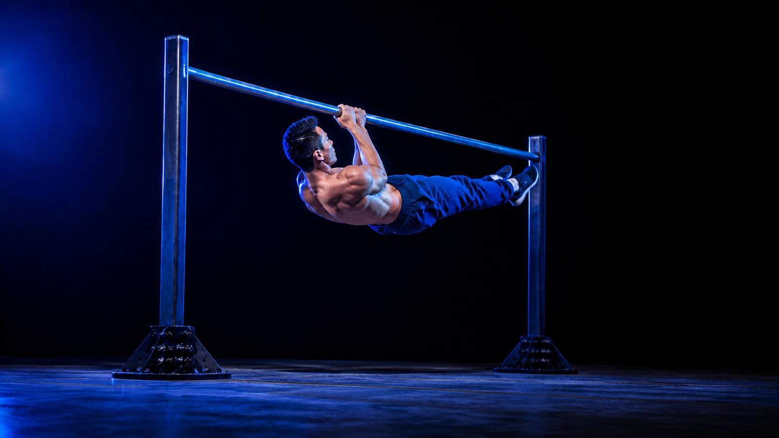 Rayan Onizuka performs a front lever pull-up with his body straight and parallel to the floor under blue stage lighting