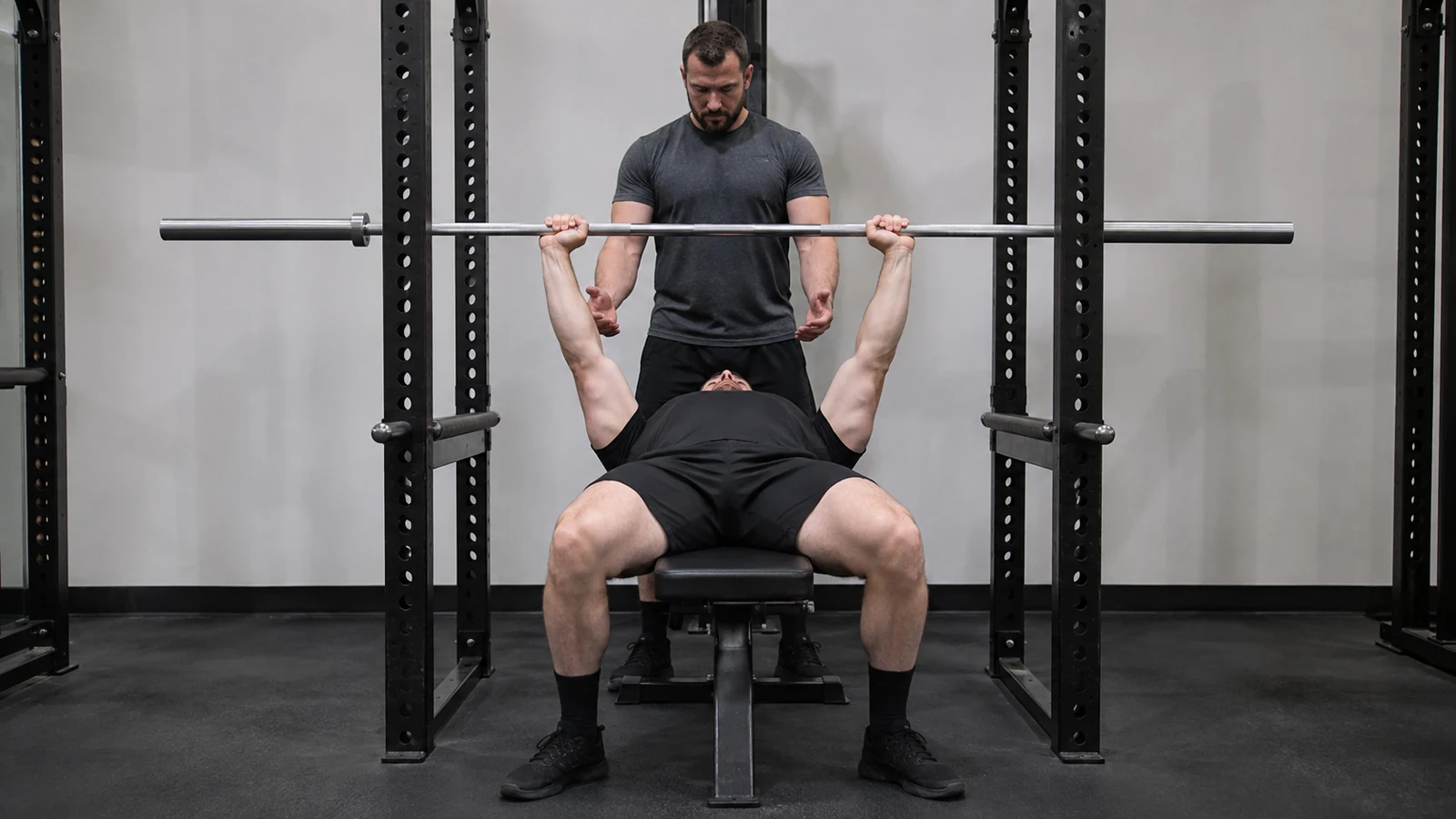 Recreational lifter practicing a repeatable raw bench setup with an attentive spotter and an empty bar.