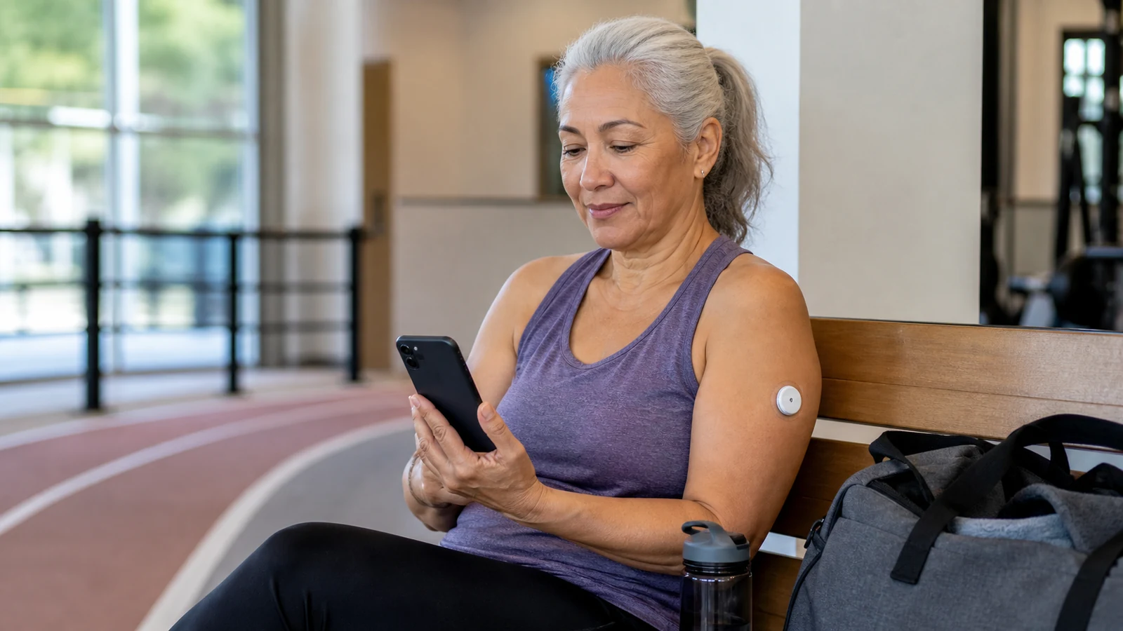 Older woman checking glucose information on her phone after exercising beside an indoor track