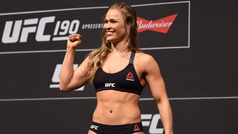 Ronda Rousey smiles and raises her fist at a UFC 190 weigh-in.