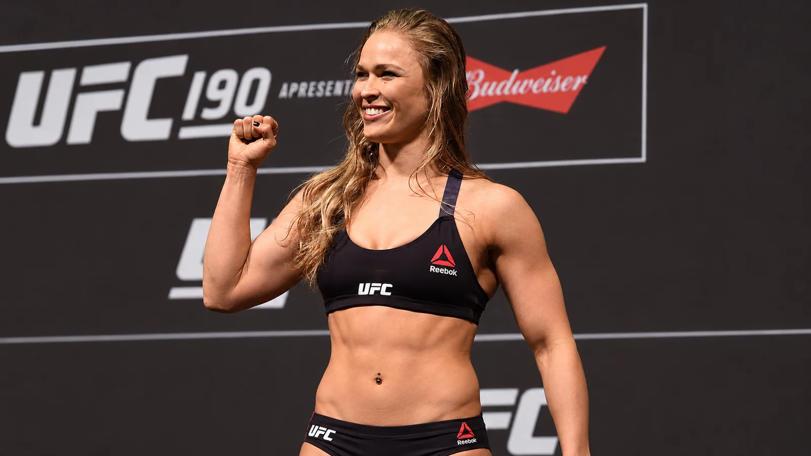 Ronda Rousey smiles and raises her fist at a UFC 190 weigh-in.