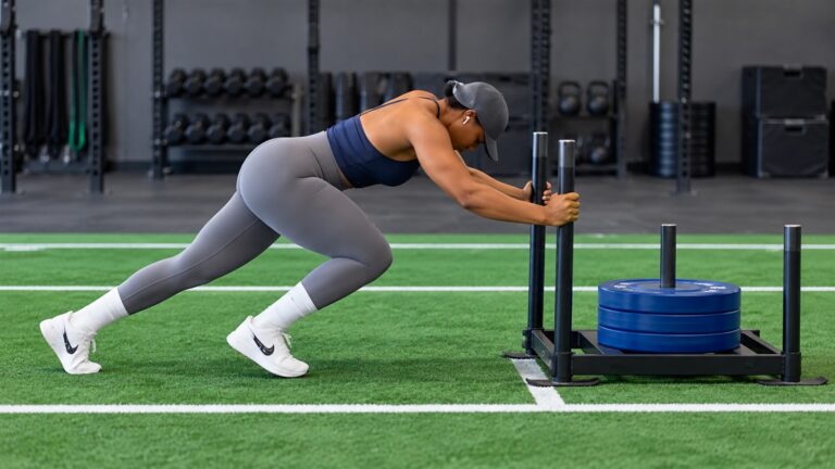 Athlete pushing a weighted sled across indoor turf with a steady forward lean